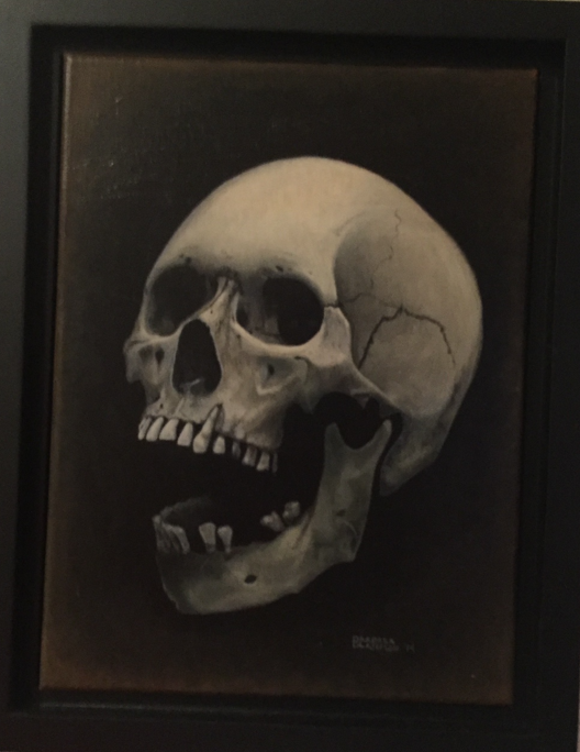 Framed painting of a human skull in a black frame